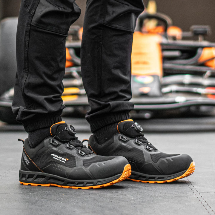 Person wearing black and orange shoes with a blurred background of a car.