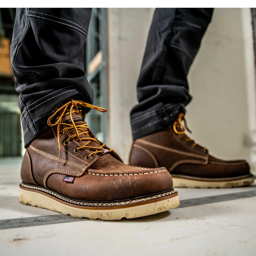 Brown leather boots with yellow laces worn by a person on a concrete floor.