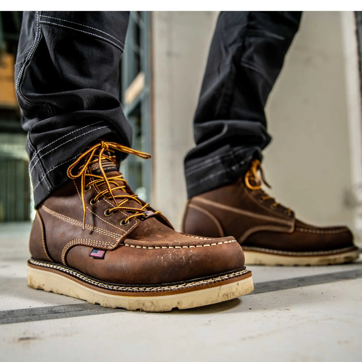Brown leather boots with yellow laces worn by a person on a concrete floor.