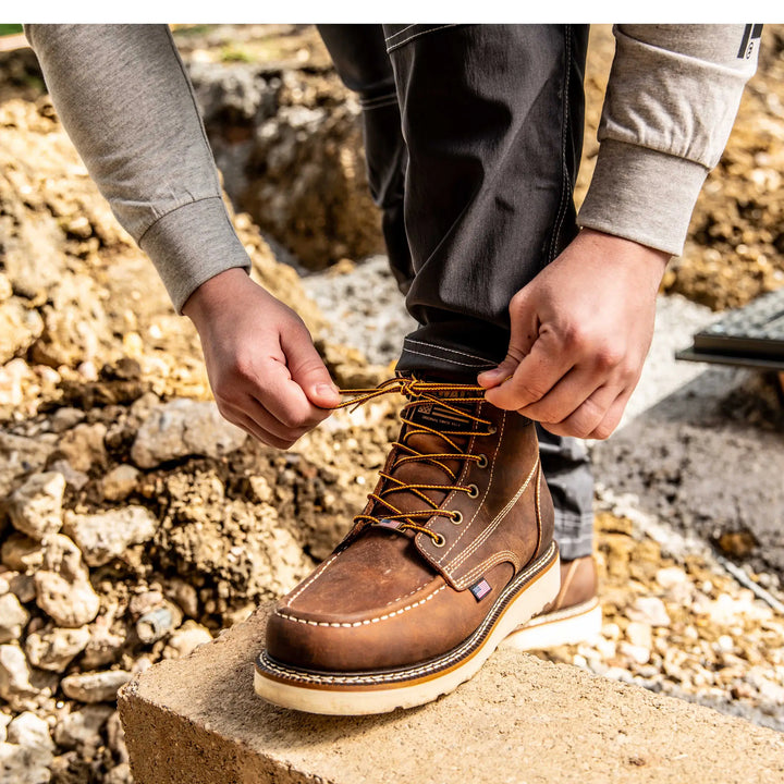 Person tying the laces of a brown leather boot outdoors.